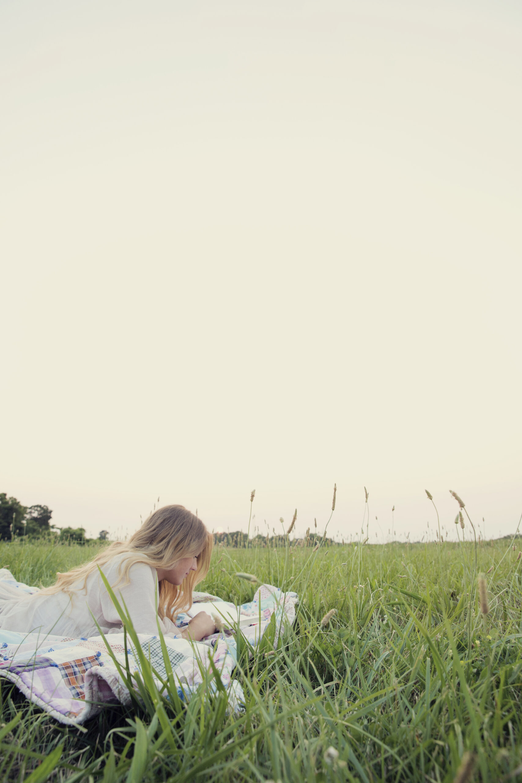 girl in field on a blanket reading